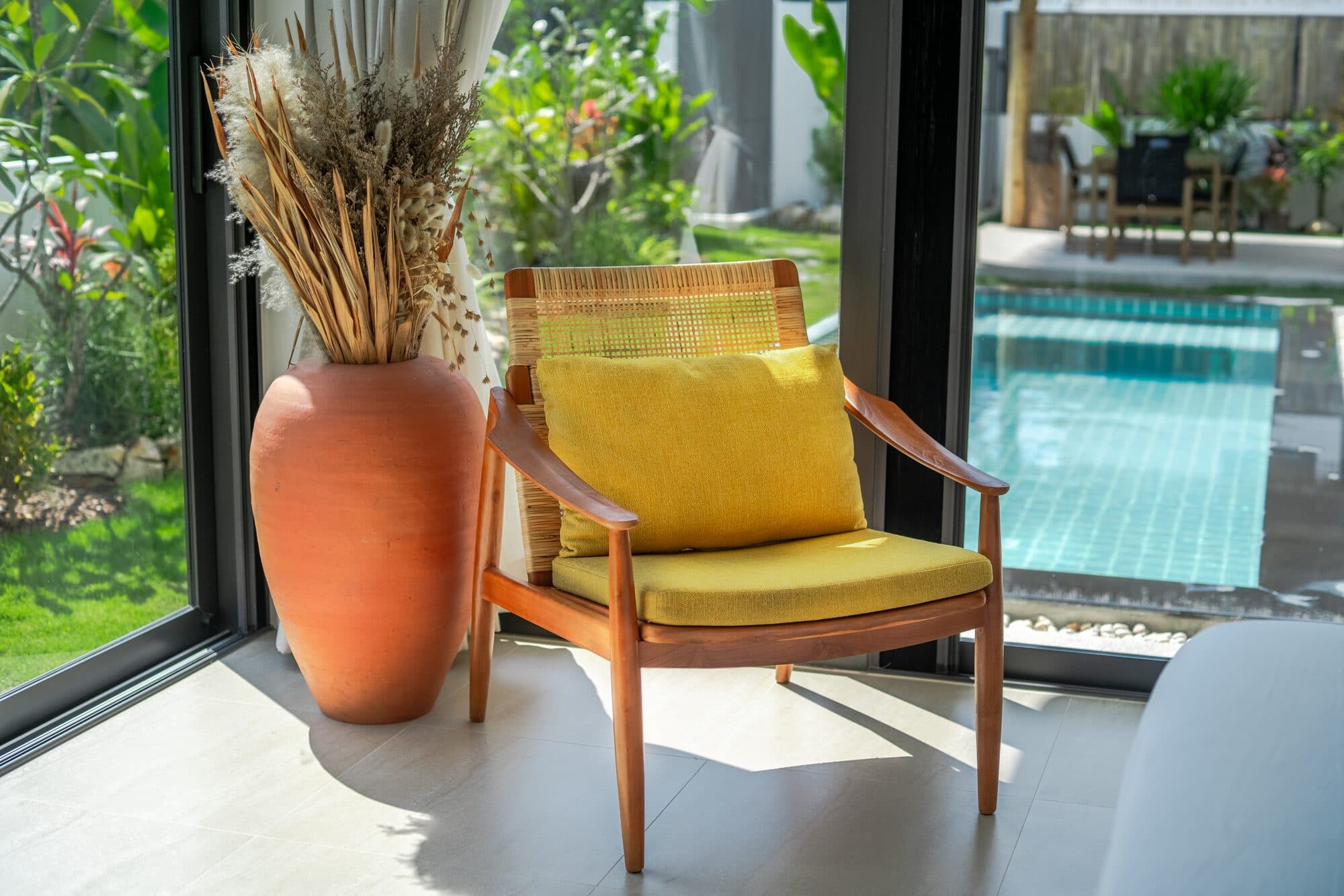 Rattan armchair with pool view through floor-to-ceiling glass — Barefoot Villas